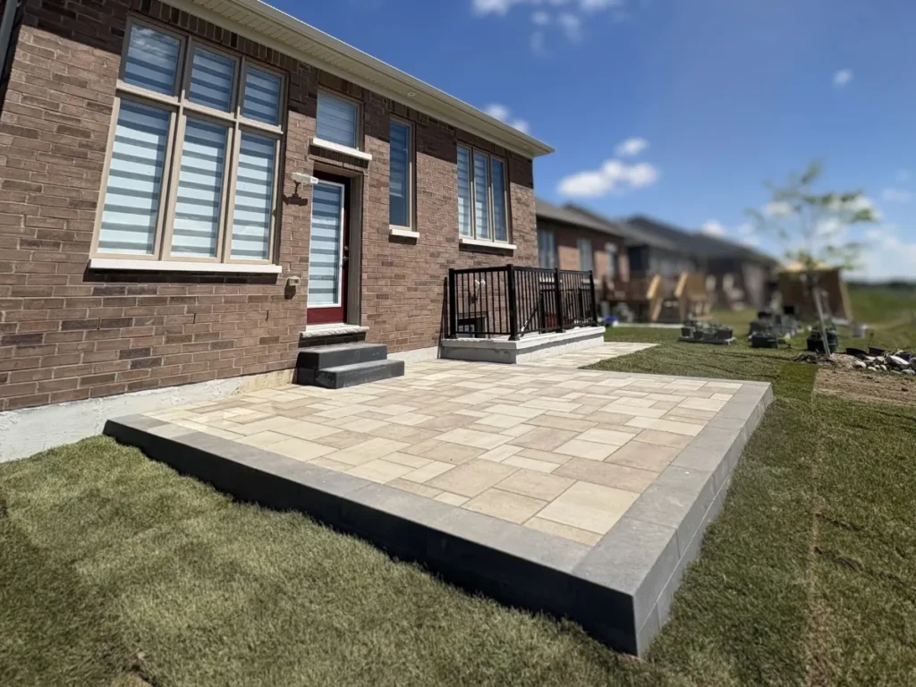 Completed hardscape project with new paver walkway, patio area, and black railing beside a brick home