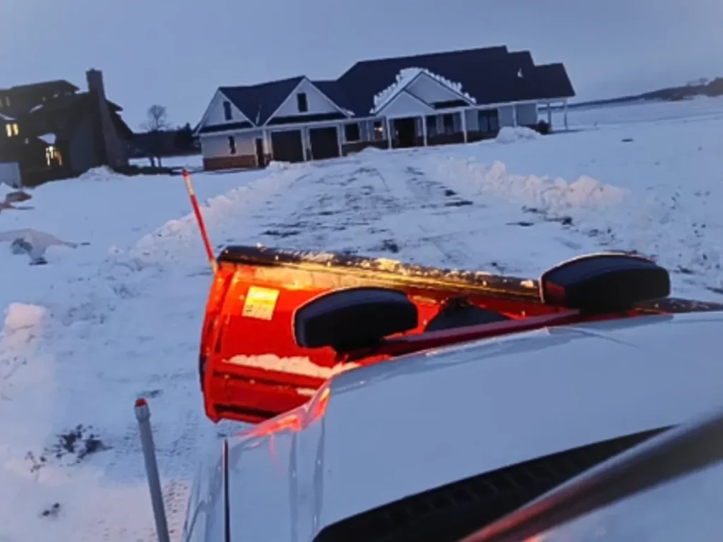 White dually truck plowing snow in a residential driveway.