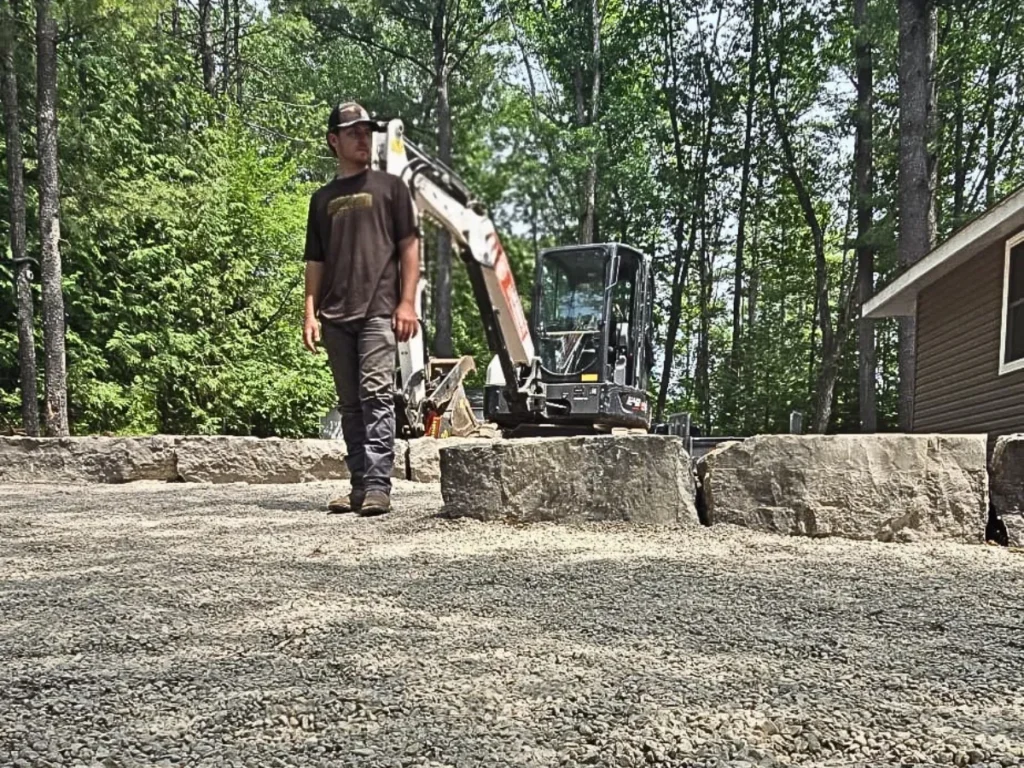 Colten Gunson standing on a rock and gravel landscape project with Big G equipment in the background.