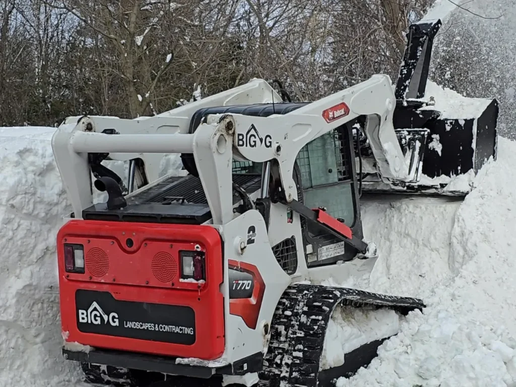 Skid steer snow blowing snow outside a commercial building.