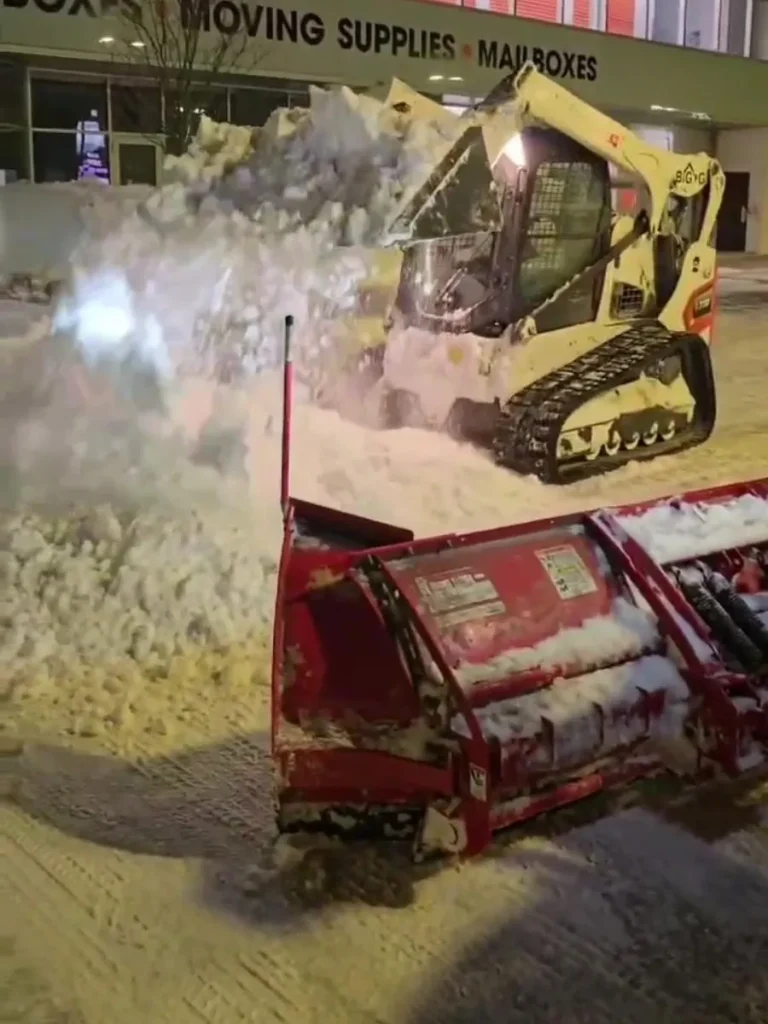 Skid steer loading and moving snow in a large snow pile.